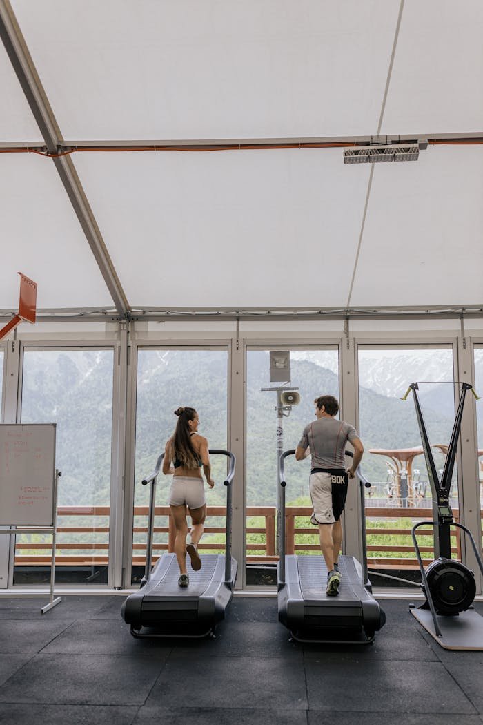 Contact Back view of a couple running on treadmills in a gym with a scenic mountain view.
