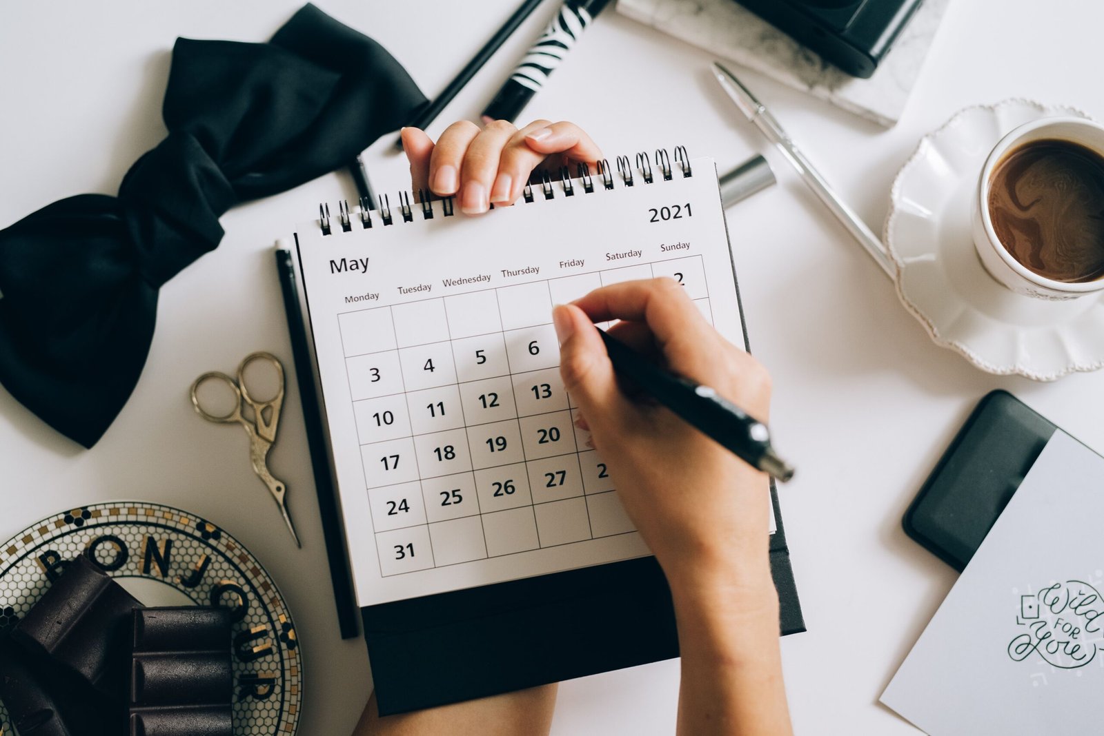 Top view of hands a planner with coffee accessories, focused on May 2021 calendar.